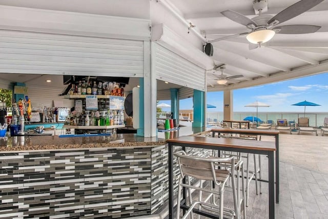 view of patio featuring ceiling fan, a water view, and exterior bar