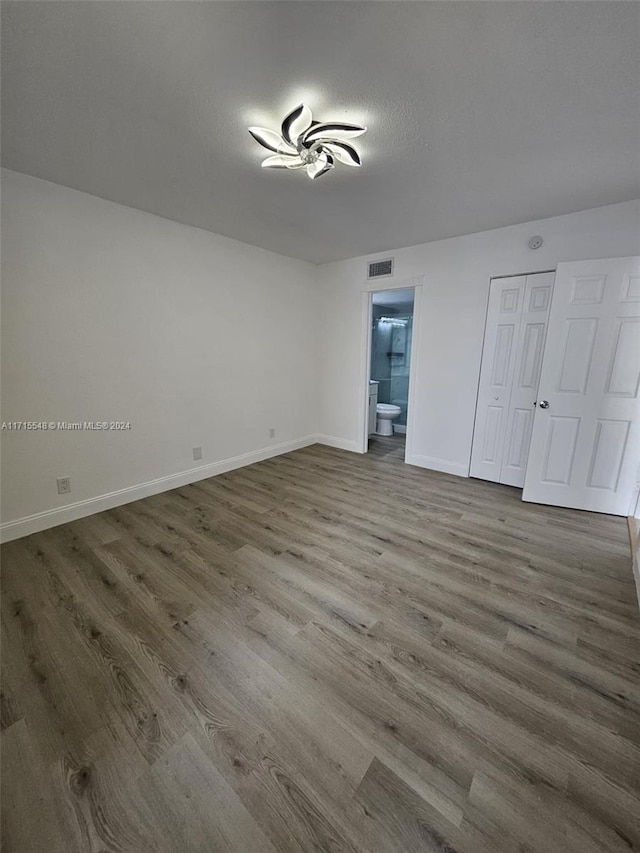 unfurnished bedroom with connected bathroom, a closet, wood-type flooring, and a textured ceiling