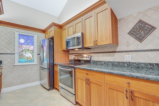 kitchen with appliances with stainless steel finishes, vaulted ceiling, light tile patterned floors, and dark stone counters