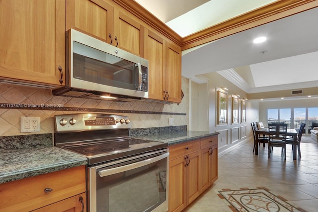 kitchen with dark stone countertops, ornamental molding, light tile patterned floors, tasteful backsplash, and stainless steel appliances