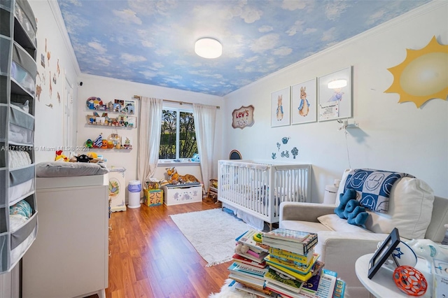 bedroom featuring hardwood / wood-style flooring, ornamental molding, and a nursery area