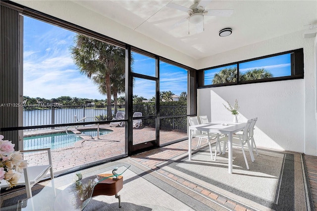 sunroom with ceiling fan and a water view