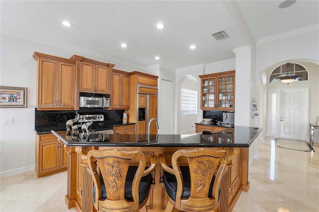 kitchen featuring paneled built in fridge, a kitchen breakfast bar, stainless steel electric range oven, a kitchen island with sink, and crown molding