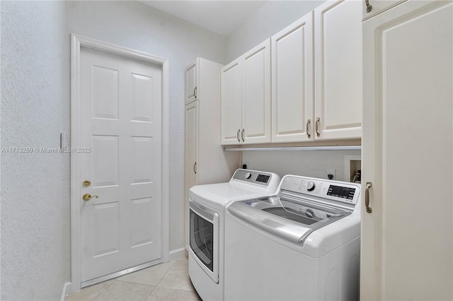 clothes washing area with washing machine and dryer, light tile patterned flooring, and cabinets