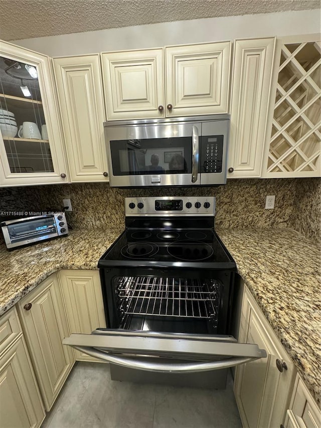 kitchen with cream cabinetry, black range with electric cooktop, tasteful backsplash, and light stone counters