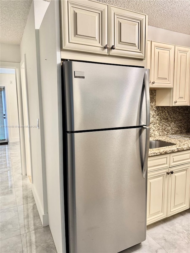 kitchen with decorative backsplash, stainless steel fridge, light stone countertops, a textured ceiling, and cream cabinetry