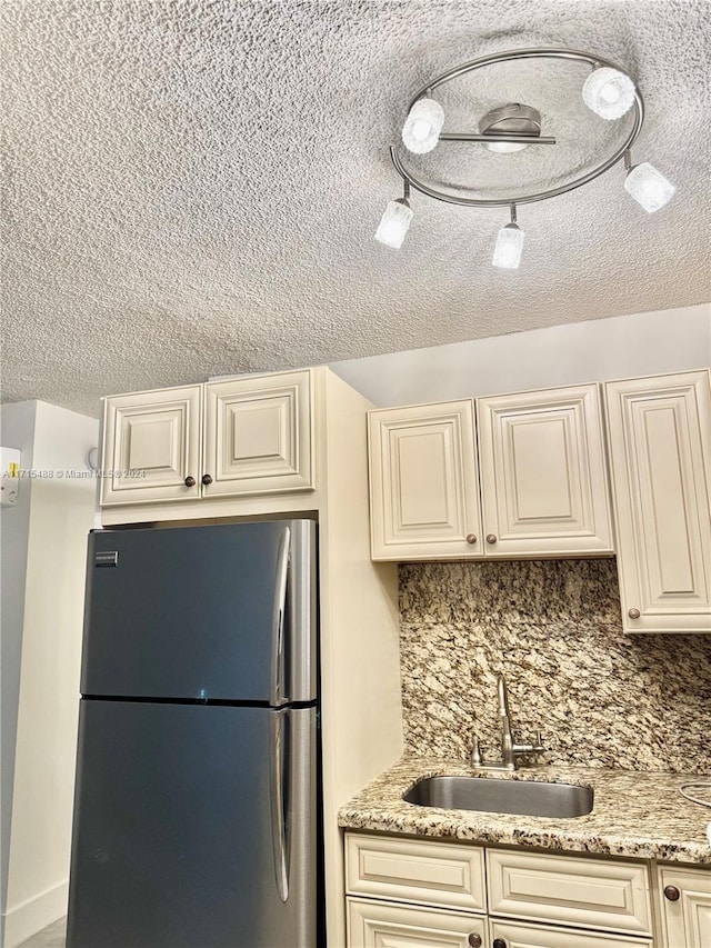 kitchen featuring tasteful backsplash, light stone counters, sink, cream cabinetry, and stainless steel refrigerator