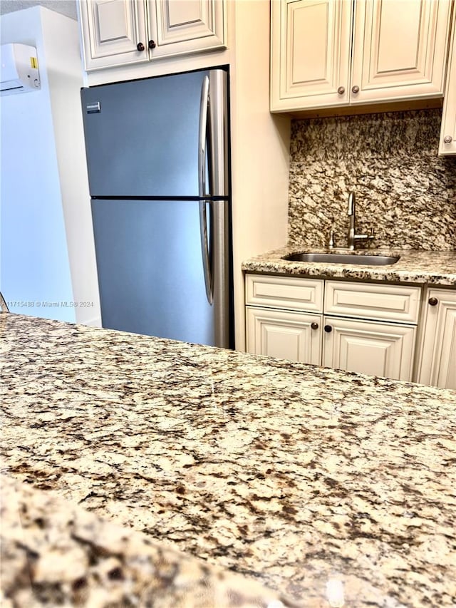 kitchen featuring backsplash, an AC wall unit, sink, stainless steel fridge, and light stone counters