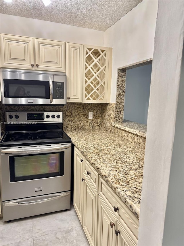 kitchen featuring cream cabinetry, light stone counters, a textured ceiling, and appliances with stainless steel finishes