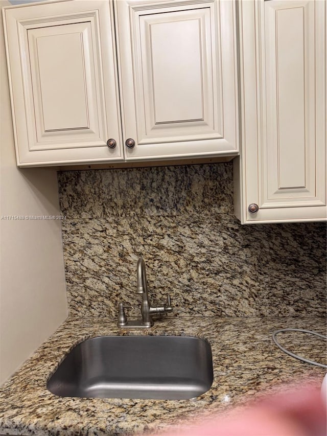 kitchen with stone countertops, white cabinetry, decorative backsplash, and sink