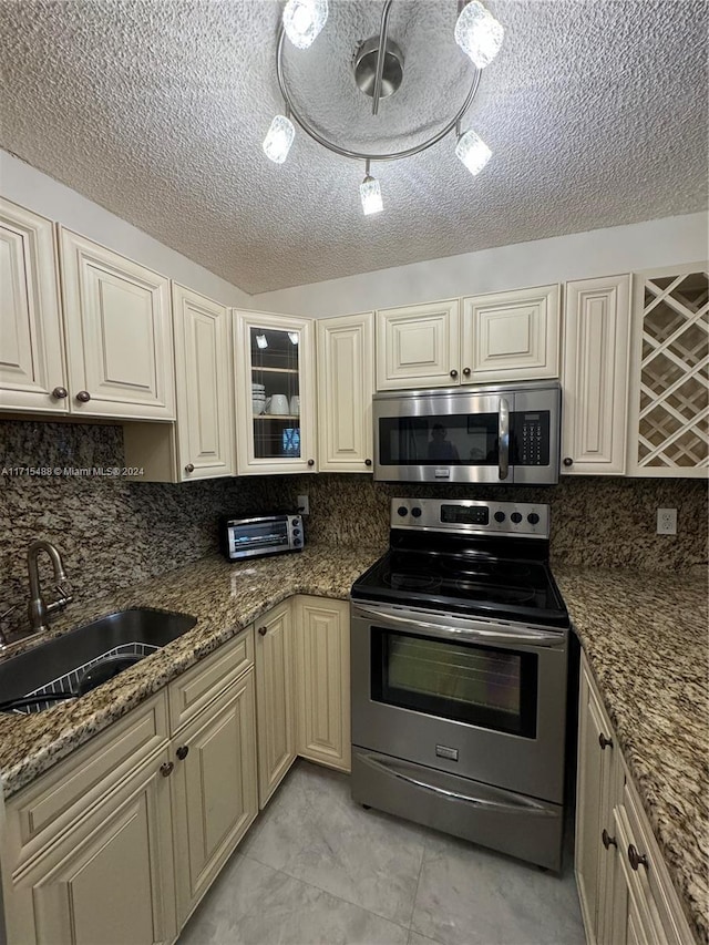 kitchen featuring sink, stainless steel appliances, tasteful backsplash, dark stone countertops, and cream cabinetry