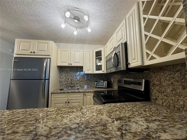 kitchen featuring stone counters, sink, backsplash, a textured ceiling, and appliances with stainless steel finishes