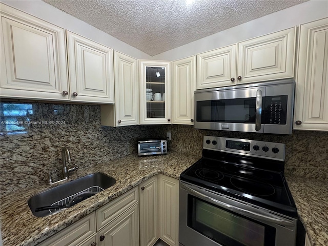 kitchen featuring decorative backsplash, appliances with stainless steel finishes, dark stone counters, and sink