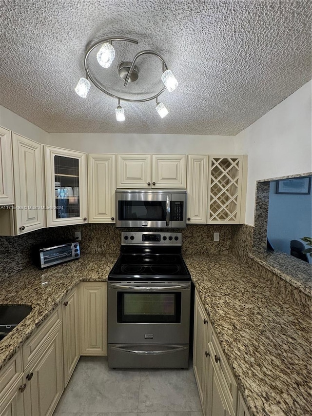 kitchen with backsplash, dark stone countertops, light tile patterned floors, appliances with stainless steel finishes, and cream cabinetry