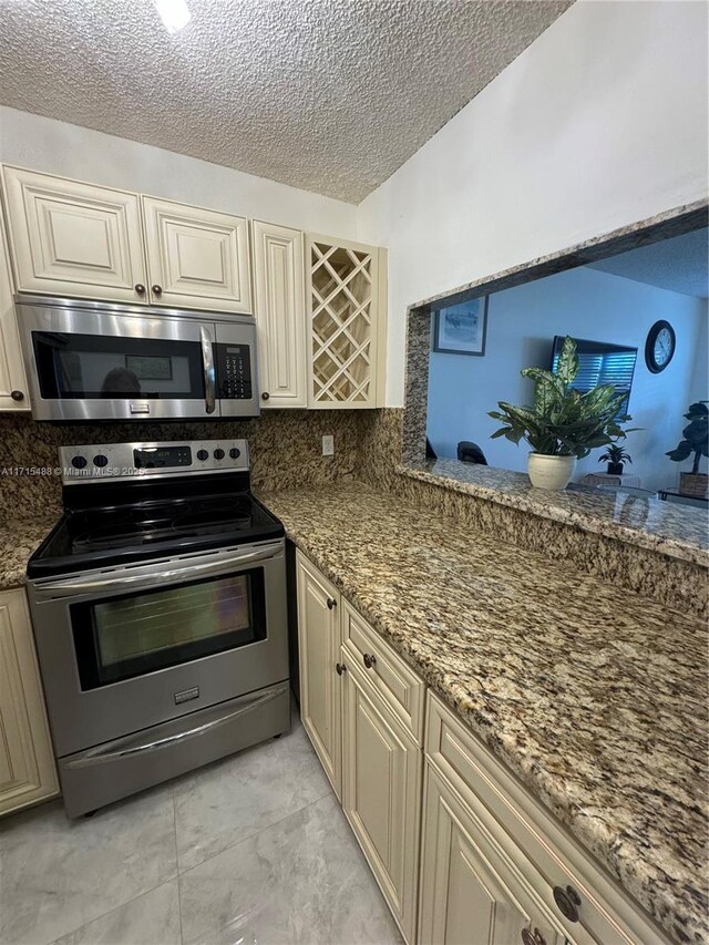 kitchen featuring tasteful backsplash, cream cabinets, stone countertops, and appliances with stainless steel finishes