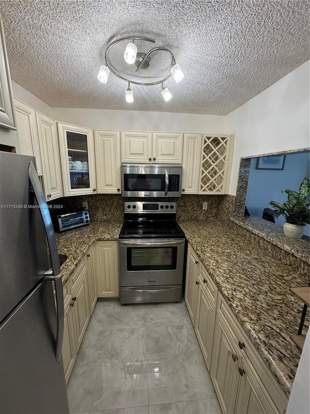 kitchen with decorative backsplash, cream cabinetry, stainless steel appliances, and dark stone counters