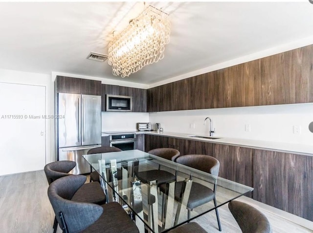 kitchen with kitchen peninsula, light wood-type flooring, stainless steel appliances, sink, and a chandelier