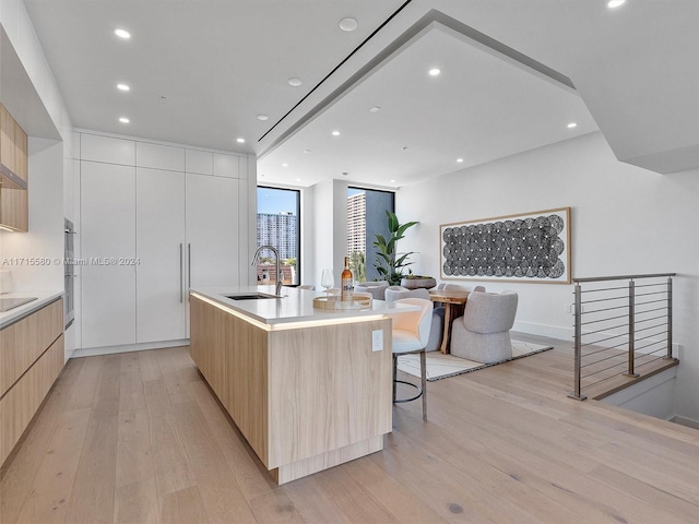 kitchen with light wood-type flooring, a large island, sink, white cabinetry, and a breakfast bar area