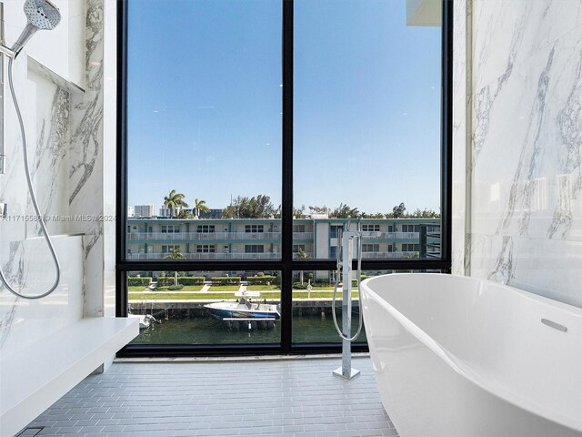 interior space featuring plenty of natural light, a water view, a wall of windows, and a tub