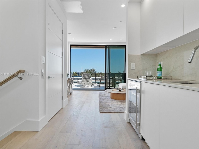 interior space with floor to ceiling windows, sink, beverage cooler, and light hardwood / wood-style floors