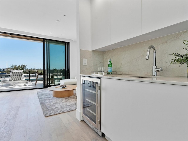 kitchen featuring sink, beverage cooler, expansive windows, backsplash, and white cabinets