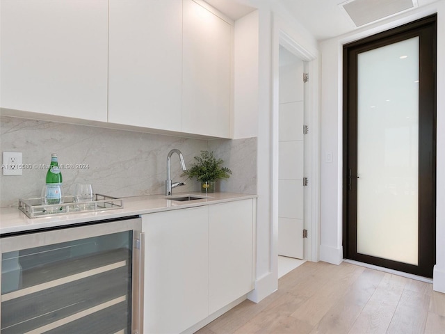 bar with backsplash, light hardwood / wood-style floors, white cabinetry, and beverage cooler