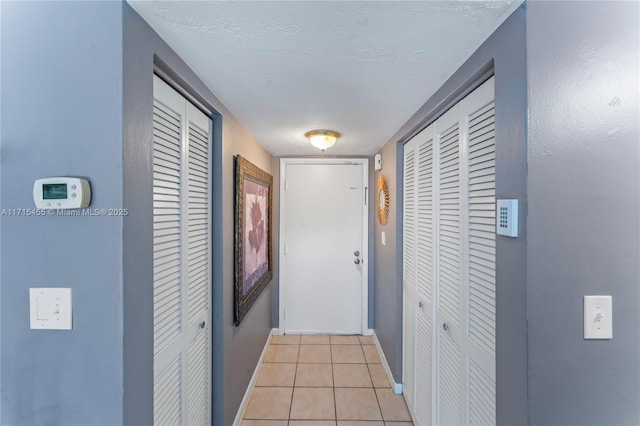 hall with baseboards, a textured ceiling, and light tile patterned flooring