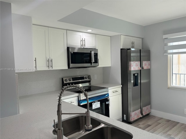 kitchen with sink, stainless steel appliances, white cabinets, and light wood-type flooring