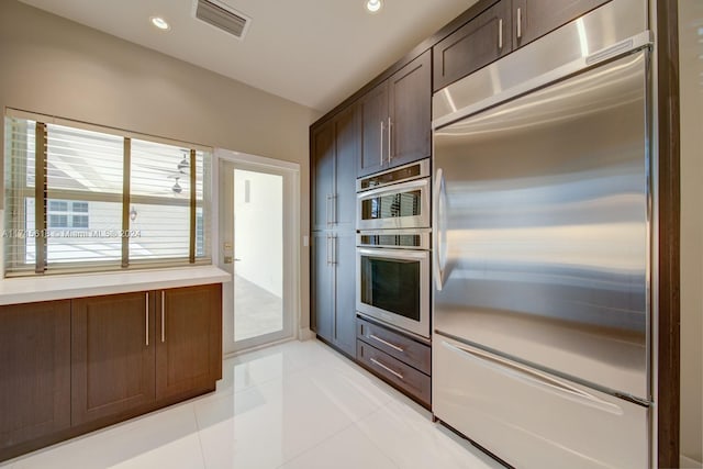 kitchen with light tile patterned floors, stainless steel appliances, and dark brown cabinets