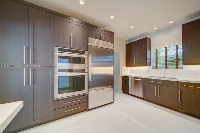 kitchen featuring sink, light tile patterned flooring, dark brown cabinets, and appliances with stainless steel finishes