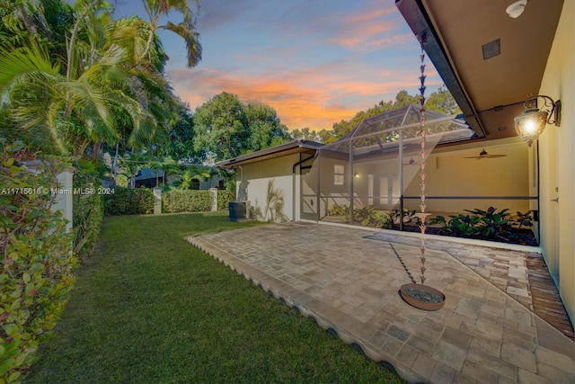 yard at dusk featuring a lanai and central AC unit