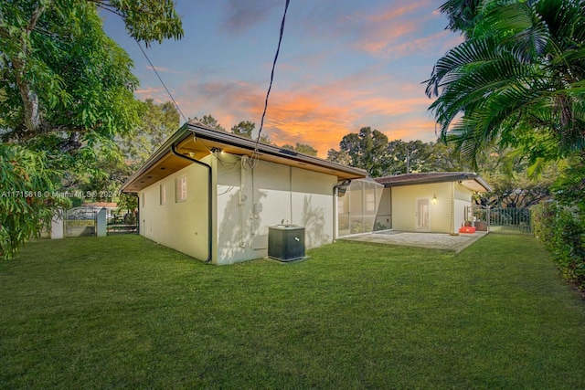 back house at dusk featuring a lawn, a patio, and central AC unit