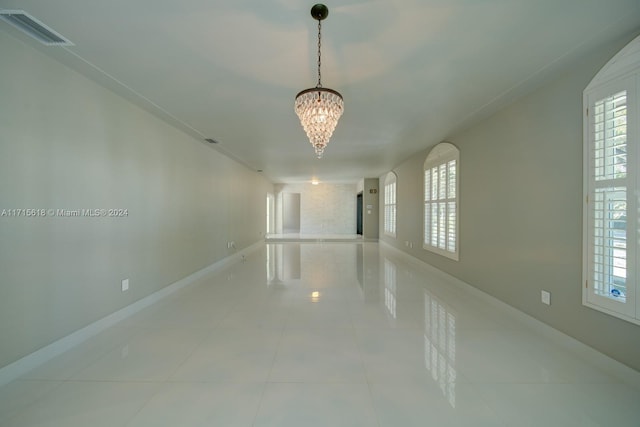 spare room with light tile patterned floors, a healthy amount of sunlight, and an inviting chandelier