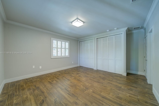 unfurnished bedroom featuring multiple closets, crown molding, and dark wood-type flooring