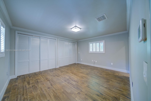 unfurnished bedroom with dark hardwood / wood-style flooring, two closets, and ornamental molding