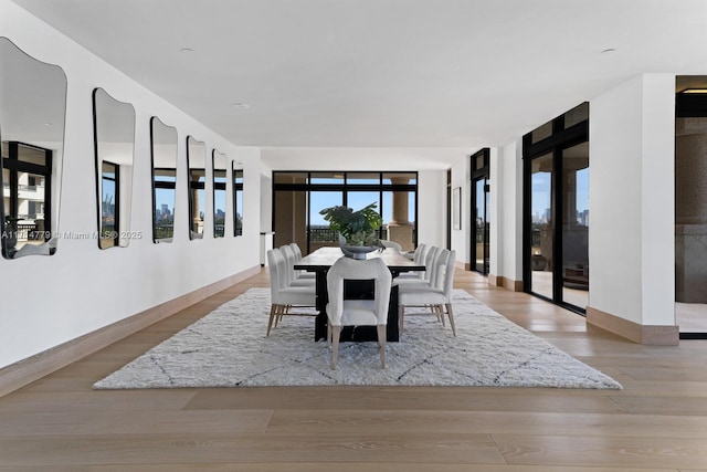 dining space with a wall of windows, baseboards, and light wood finished floors