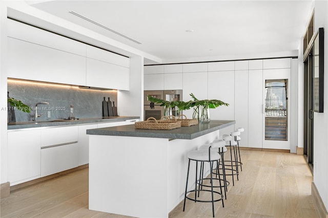 kitchen with a breakfast bar, dark countertops, light wood-style floors, white cabinetry, and modern cabinets