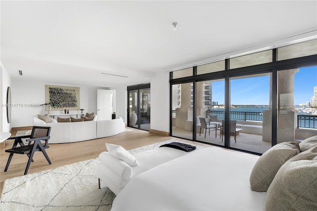 bedroom with a water view, wood finished floors, baseboards, access to outside, and floor to ceiling windows