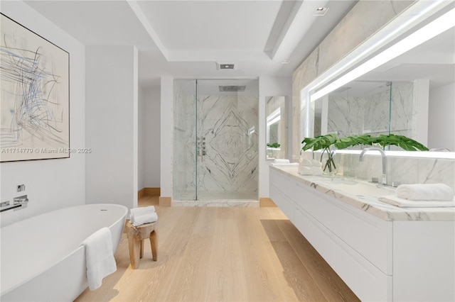 bathroom featuring a marble finish shower, double vanity, visible vents, wood finished floors, and a freestanding tub