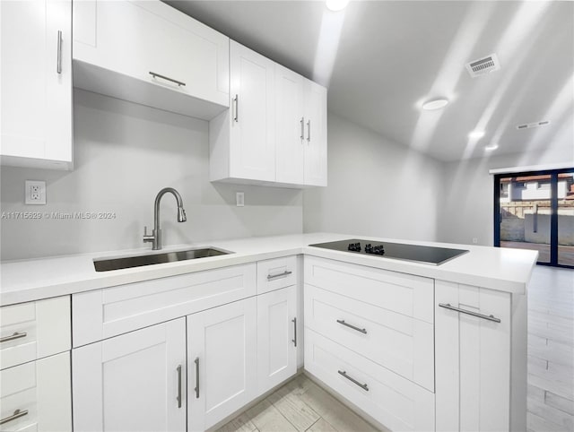 kitchen featuring white cabinets, cooktop, kitchen peninsula, and sink