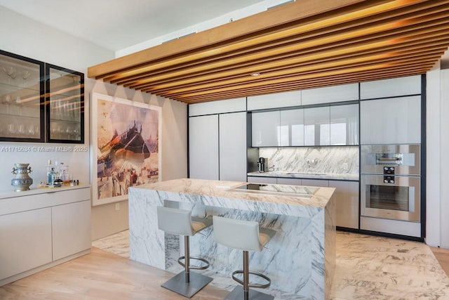 kitchen featuring a kitchen breakfast bar, tasteful backsplash, white cabinetry, and light hardwood / wood-style flooring