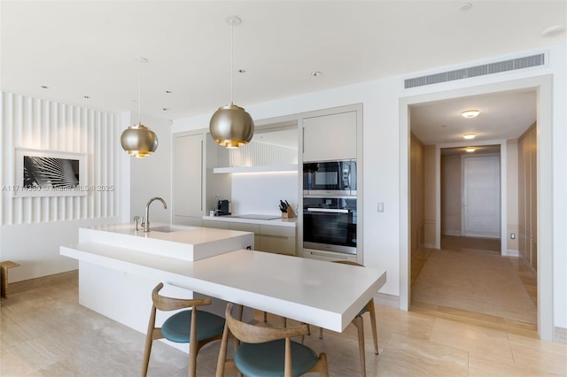 kitchen with stainless steel oven, built in microwave, sink, decorative light fixtures, and an island with sink