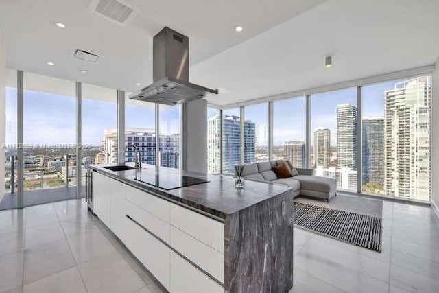 kitchen with sink, island range hood, an island with sink, white cabinets, and black electric cooktop