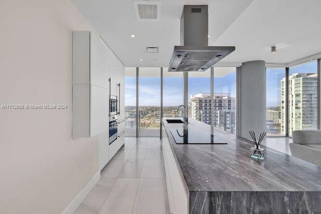 kitchen with island exhaust hood, black electric stovetop, a wall of windows, white cabinets, and oven