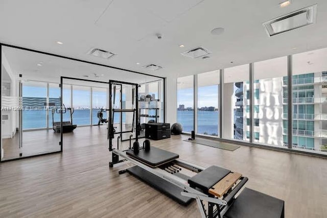 exercise room with hardwood / wood-style floors, a water view, a wall of windows, and a wealth of natural light