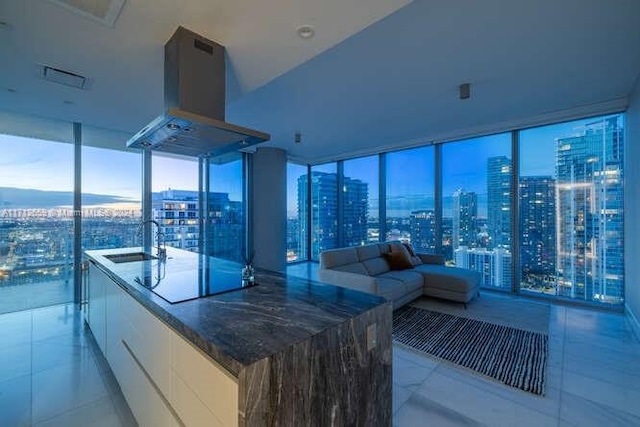 kitchen with island range hood, black electric cooktop, sink, a wall of windows, and white cabinetry