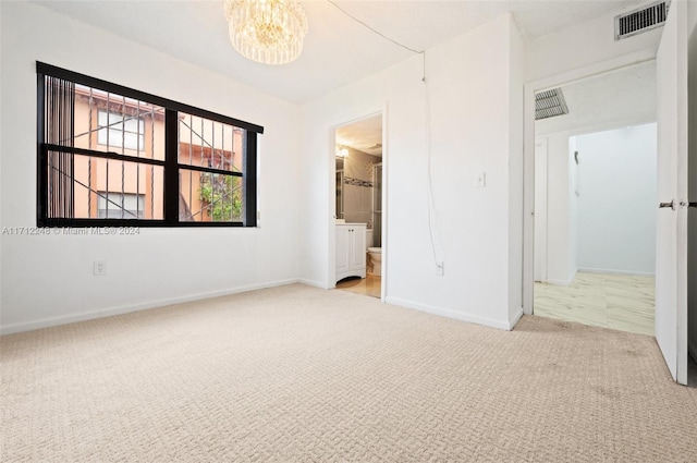 unfurnished bedroom featuring ensuite bathroom, light colored carpet, and a notable chandelier