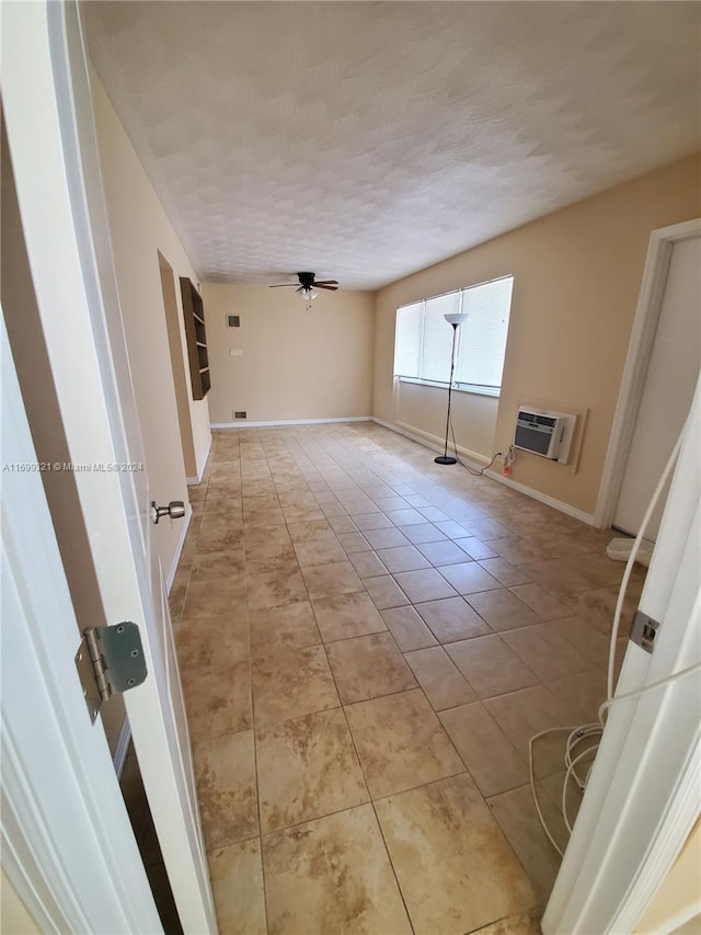 tiled spare room with ceiling fan, an AC wall unit, and a textured ceiling