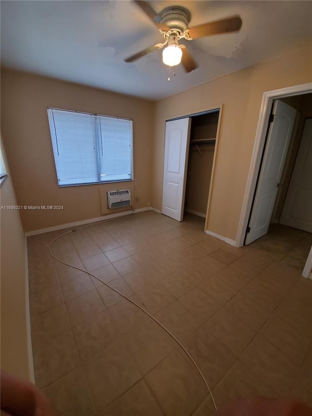 unfurnished bedroom featuring light tile patterned floors, a closet, an AC wall unit, and ceiling fan