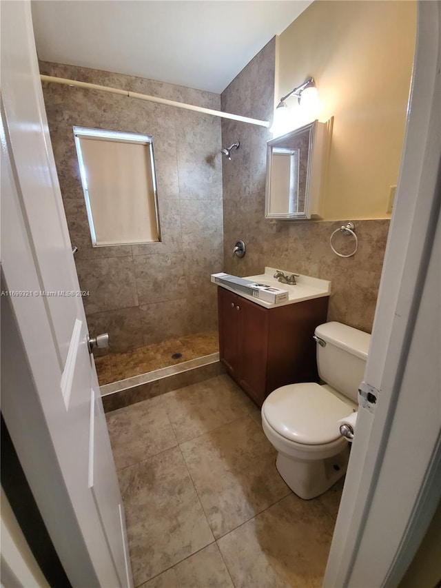 bathroom with tiled shower, vanity, toilet, and tile walls